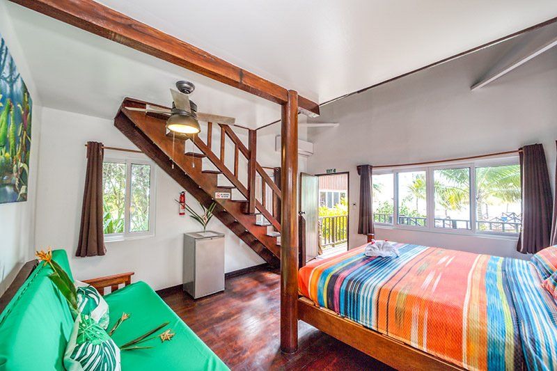 A bedroom with a bed , couch , stairs and a ceiling fan.