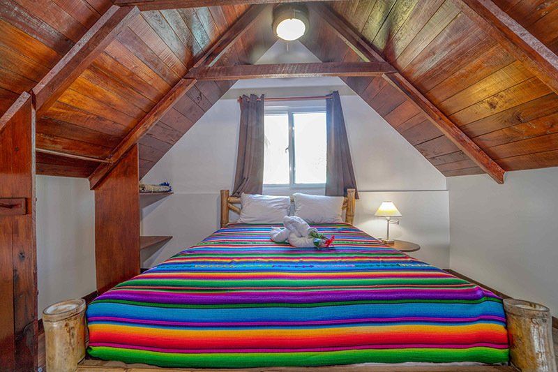 There is a bed with a colorful blanket in the attic.