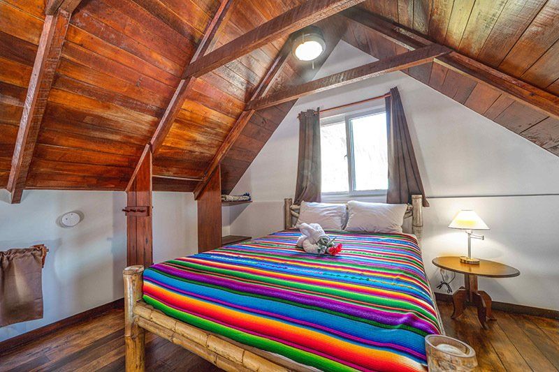 A bedroom with a wooden ceiling and a bed with a colorful blanket.