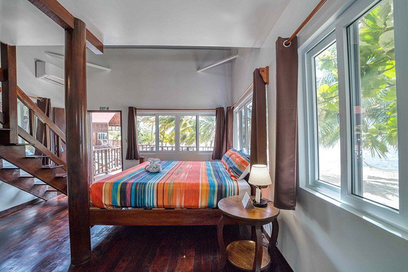 A bedroom with a king size bed , stairs , and lots of windows.