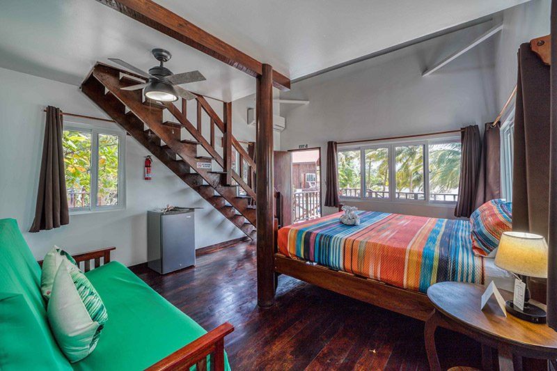 A bedroom with a king size bed , futon , stairs and a ceiling fan.