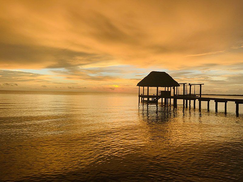 There is a dock in the middle of the ocean at sunset.