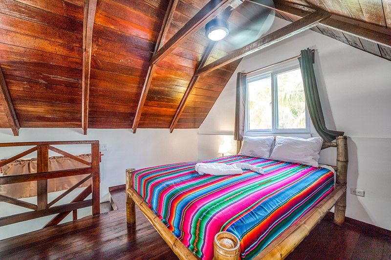A bed with a colorful blanket in a bedroom with a wooden ceiling.