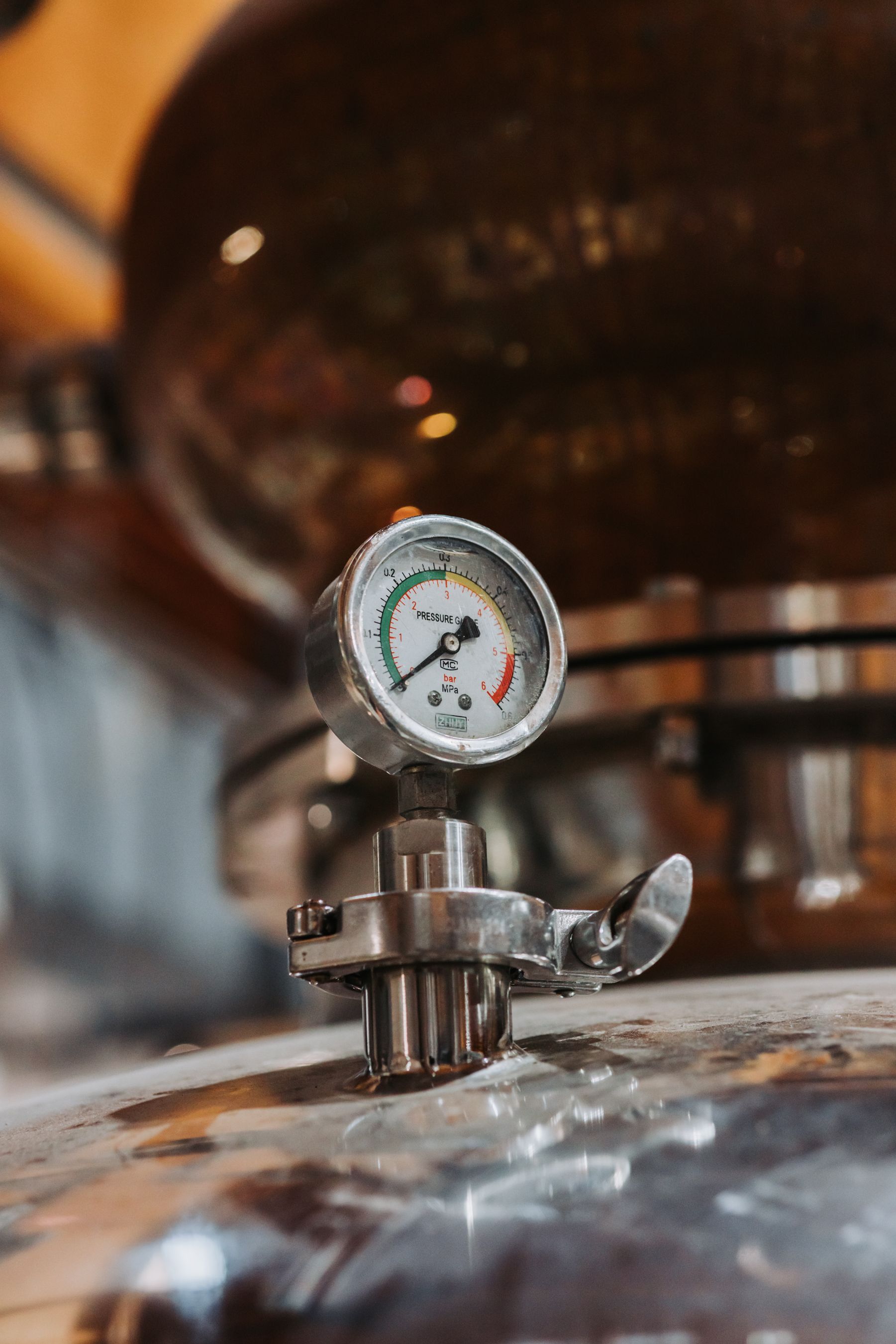 Pressure gauge on a stainless steel tank, with a reflective copper vessel in the background.