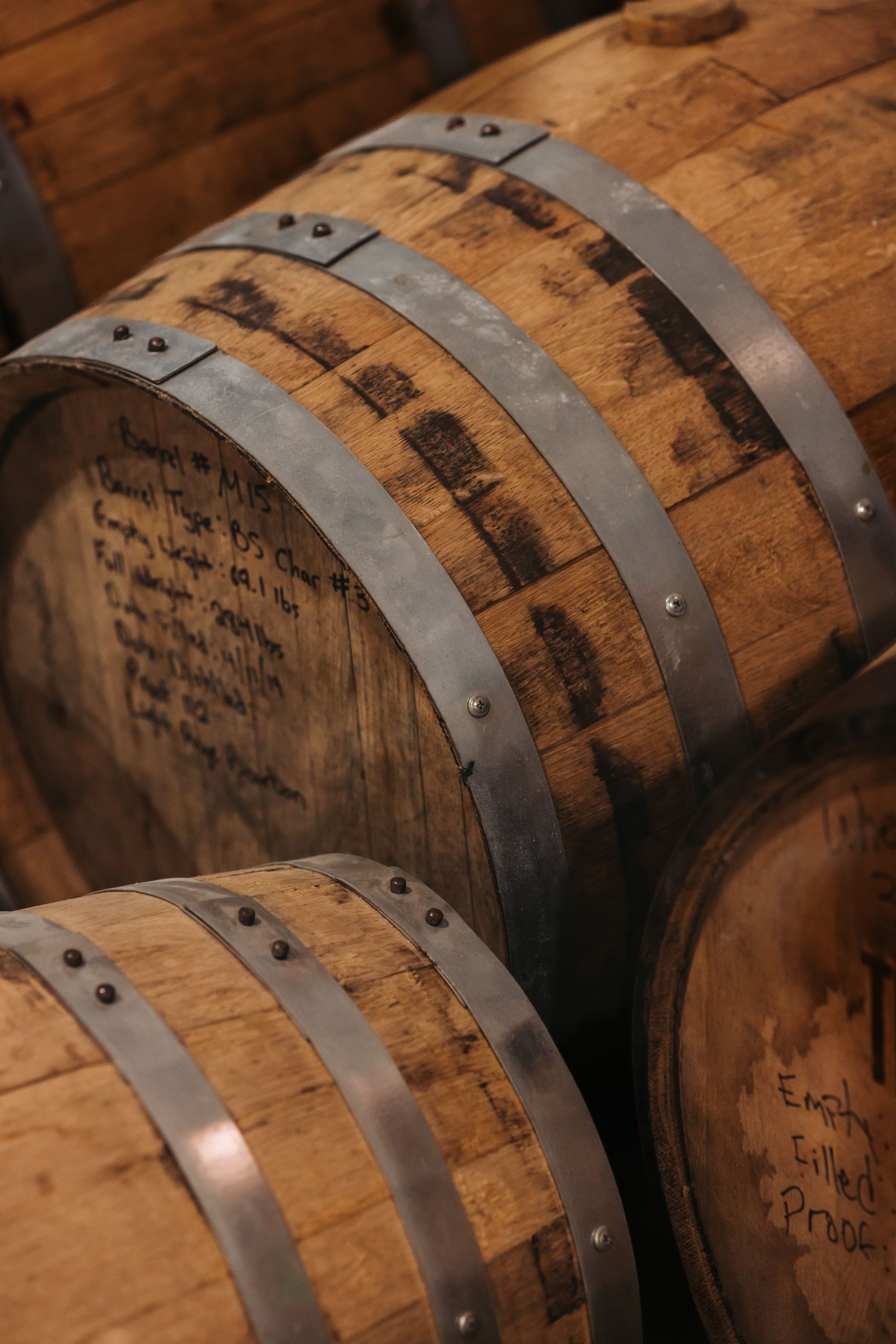 Wooden barrels with metal bands, stacked in a dimly lit setting.