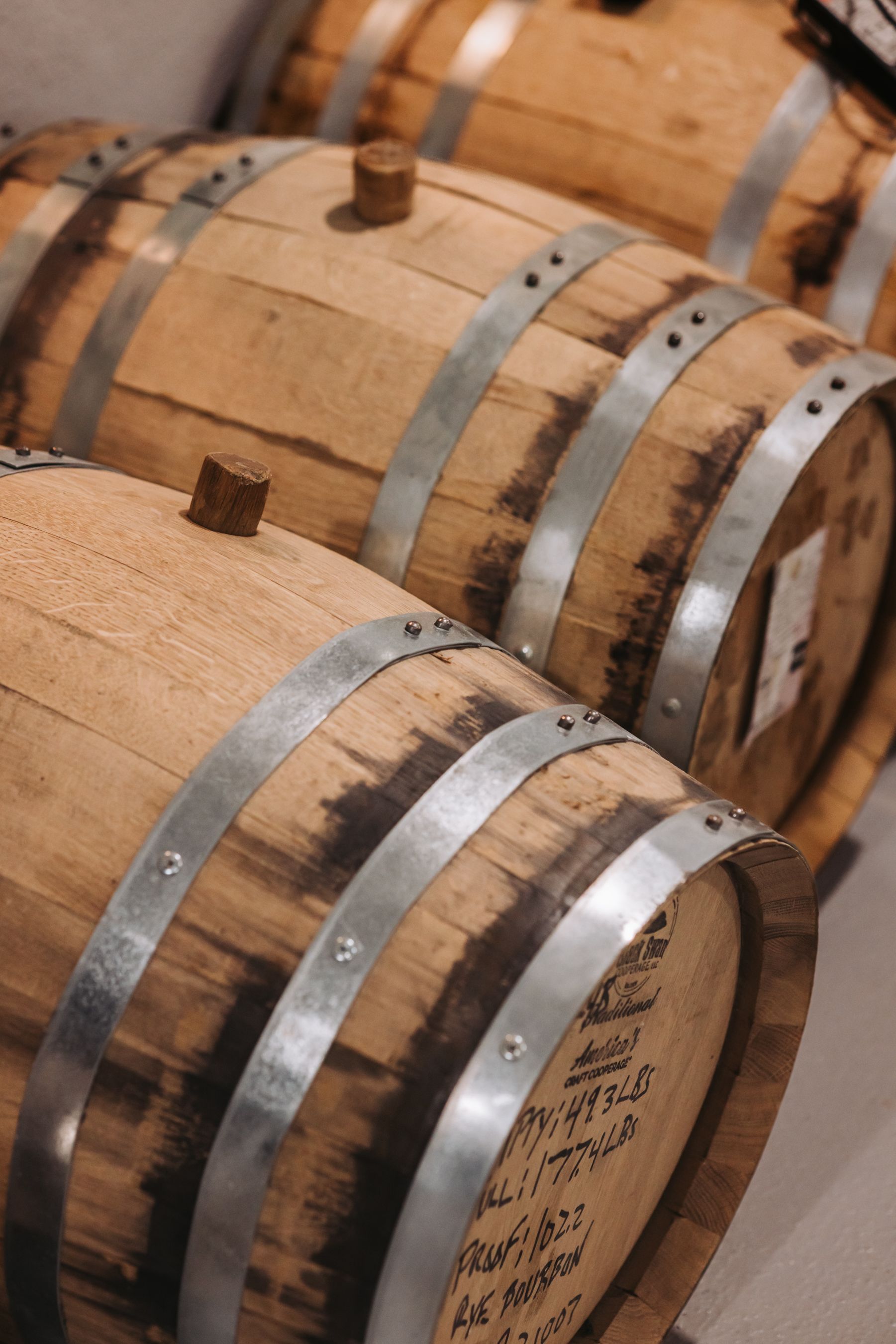 Wooden barrels with metal bands, likely for aging spirits, in a distillery or storage area.