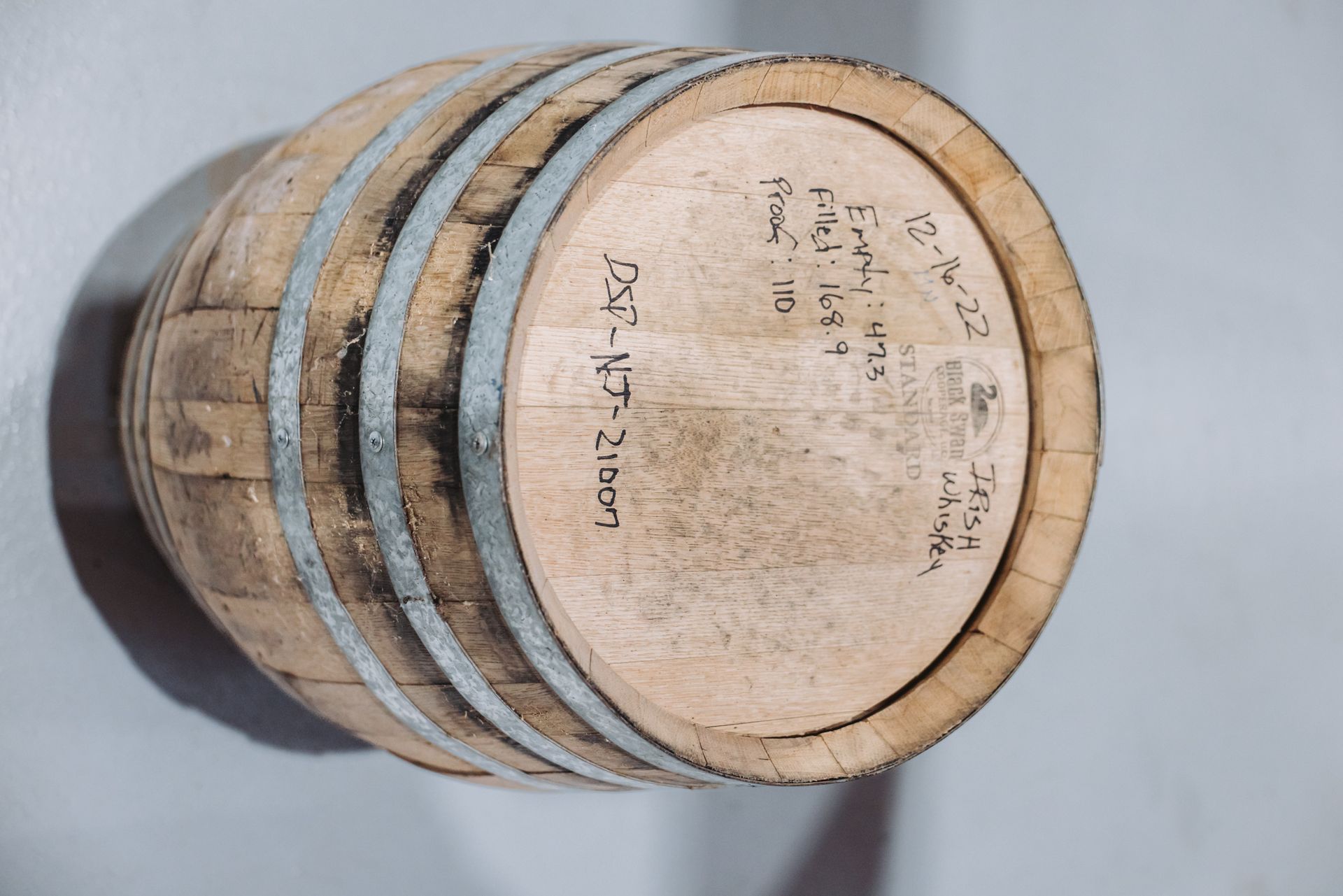 Wooden barrel with metal rings and writing on the end, resting against a white wall.