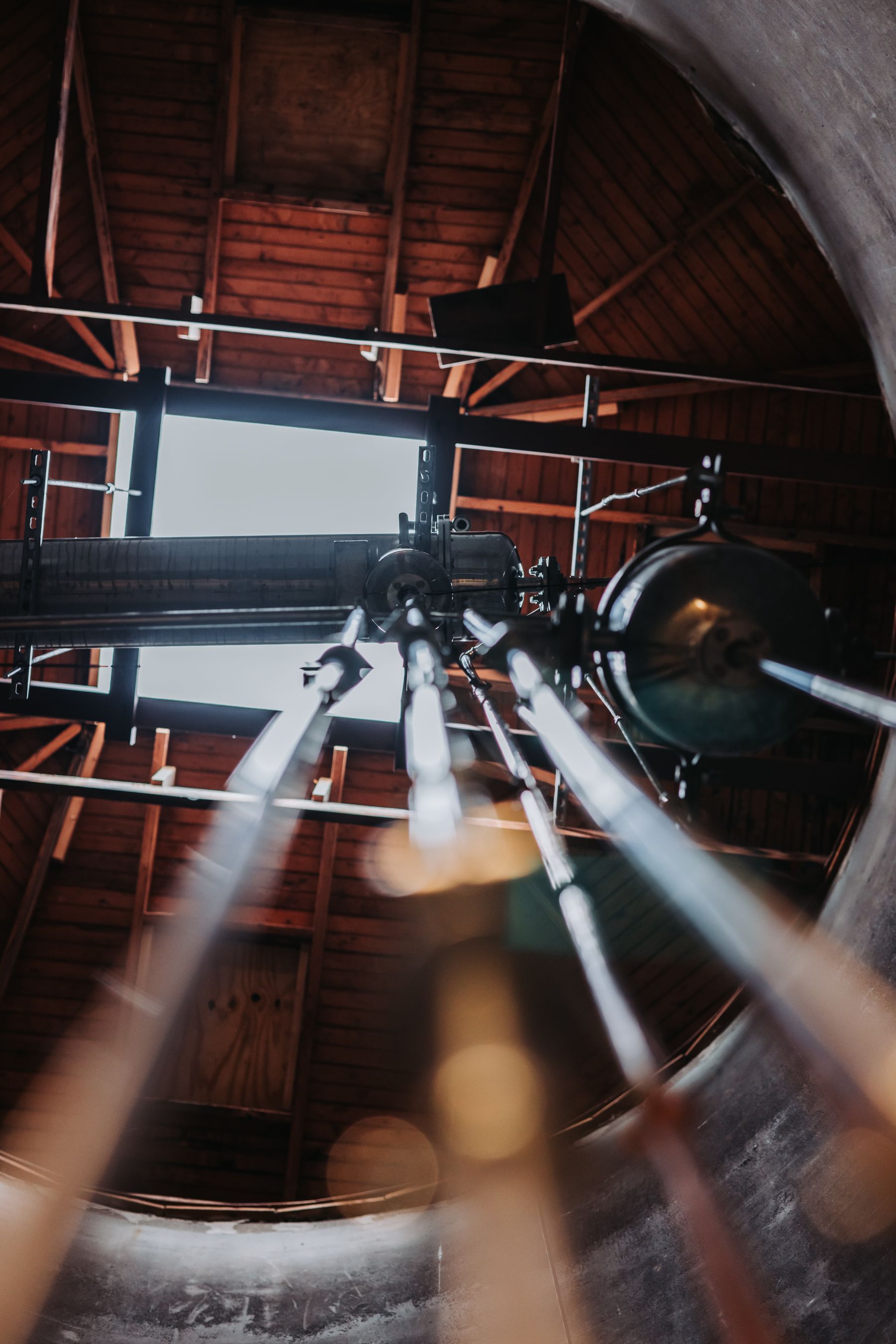 Looking up inside a cylindrical structure with pipes and machinery, wooden ceiling, and a skylight.