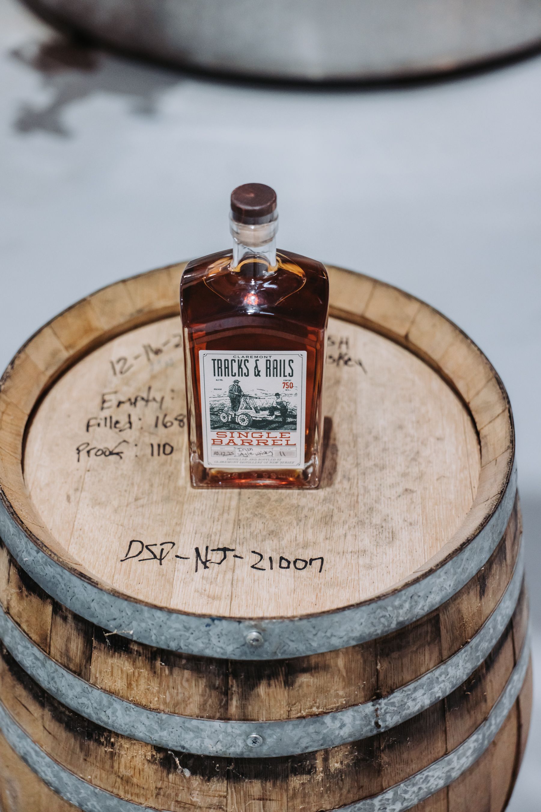 Bottle of liquor on top of a wooden barrel, with labels and markings visible.