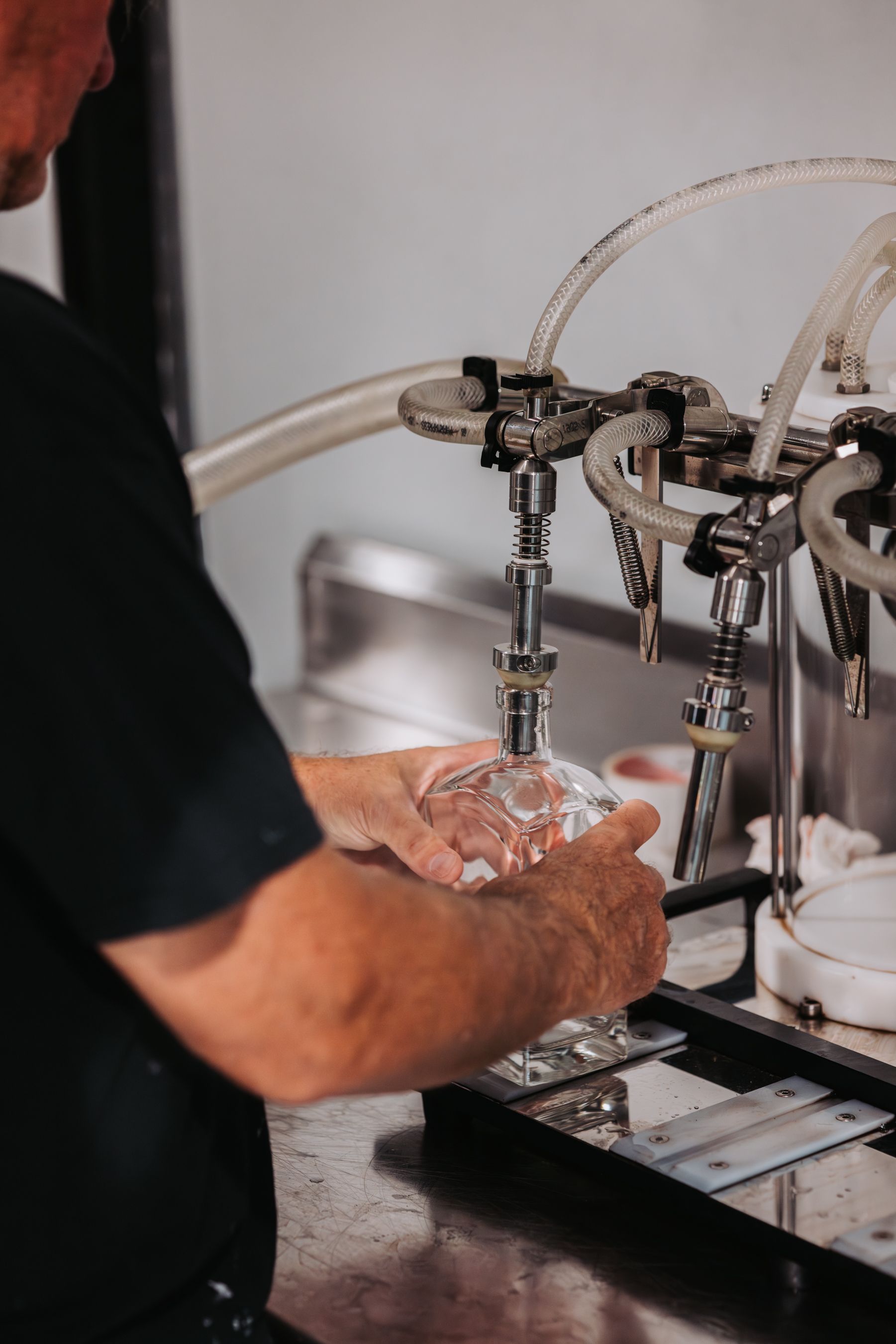 Person filling a clear glass bottle with a liquid using a machine.