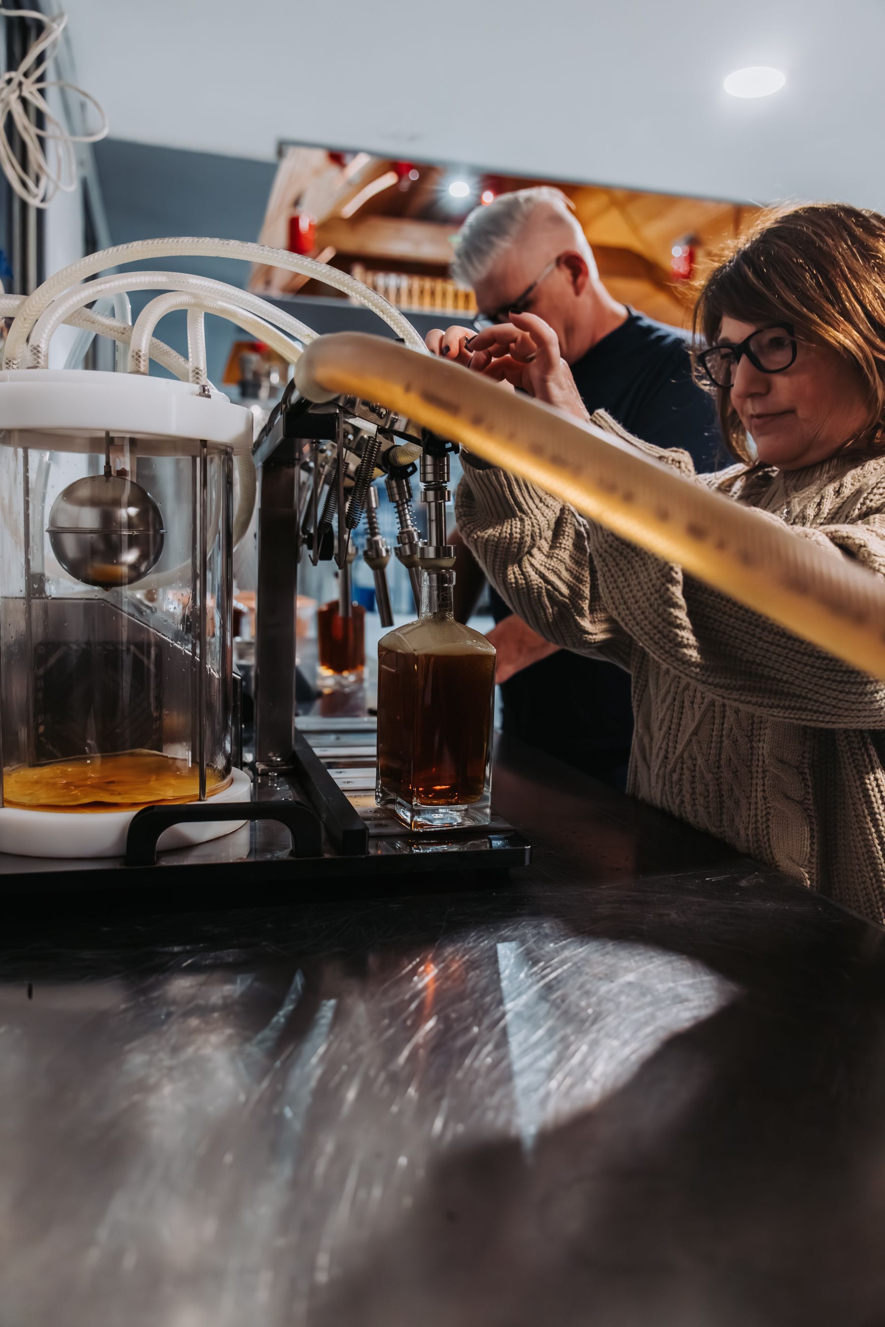 Woman pouring beer from a tap at a bar; man in background; foamy drink.