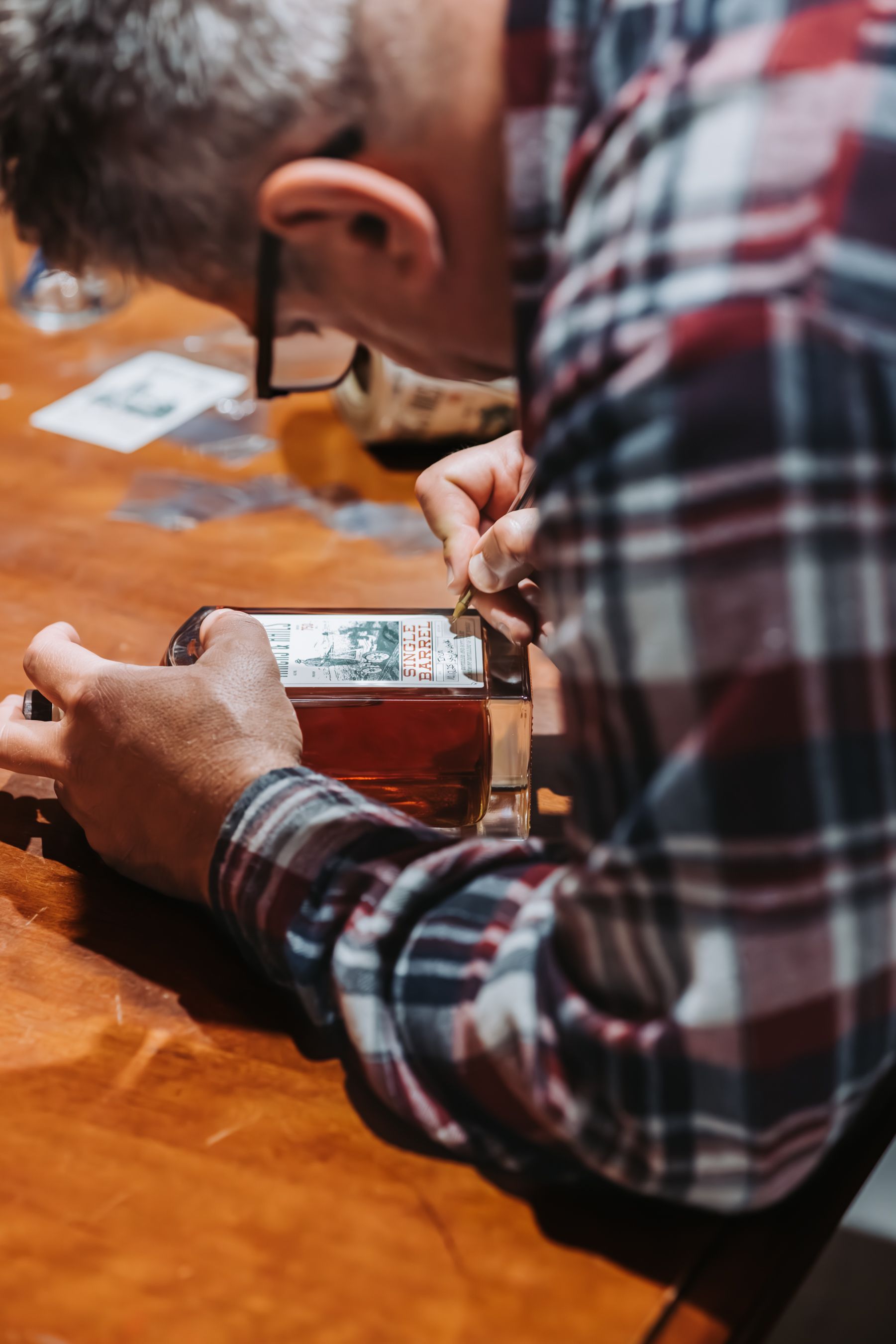 Person in plaid shirt examines a small object on a wooden table.