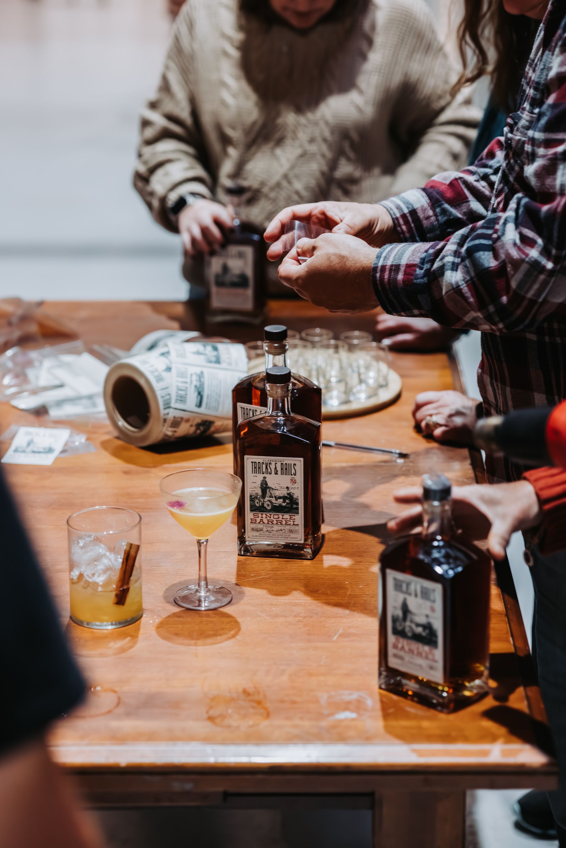 People at a table with liquor bottles and cocktails. Someone pours from a bottle.