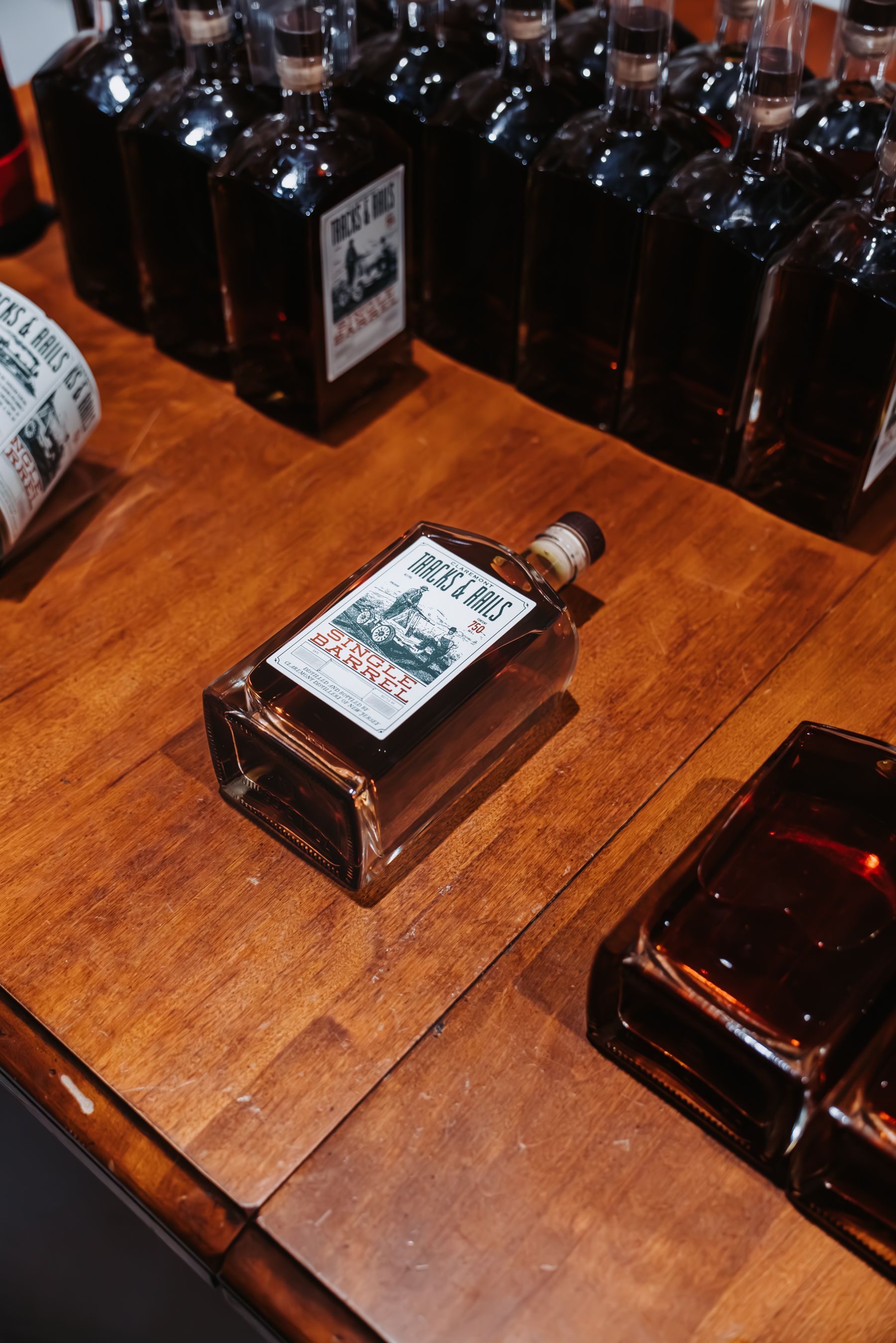 Bottles of dark liquor on a wooden table; one bottle in focus with label, others in background.