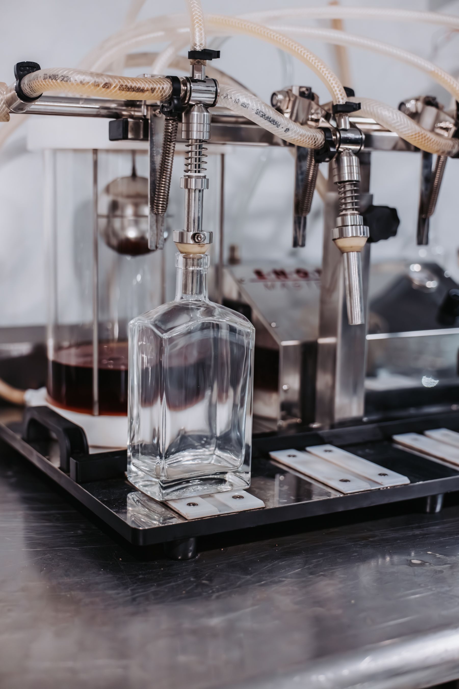 A clear glass bottle being filled with liquid by a bottling machine in a distillery.