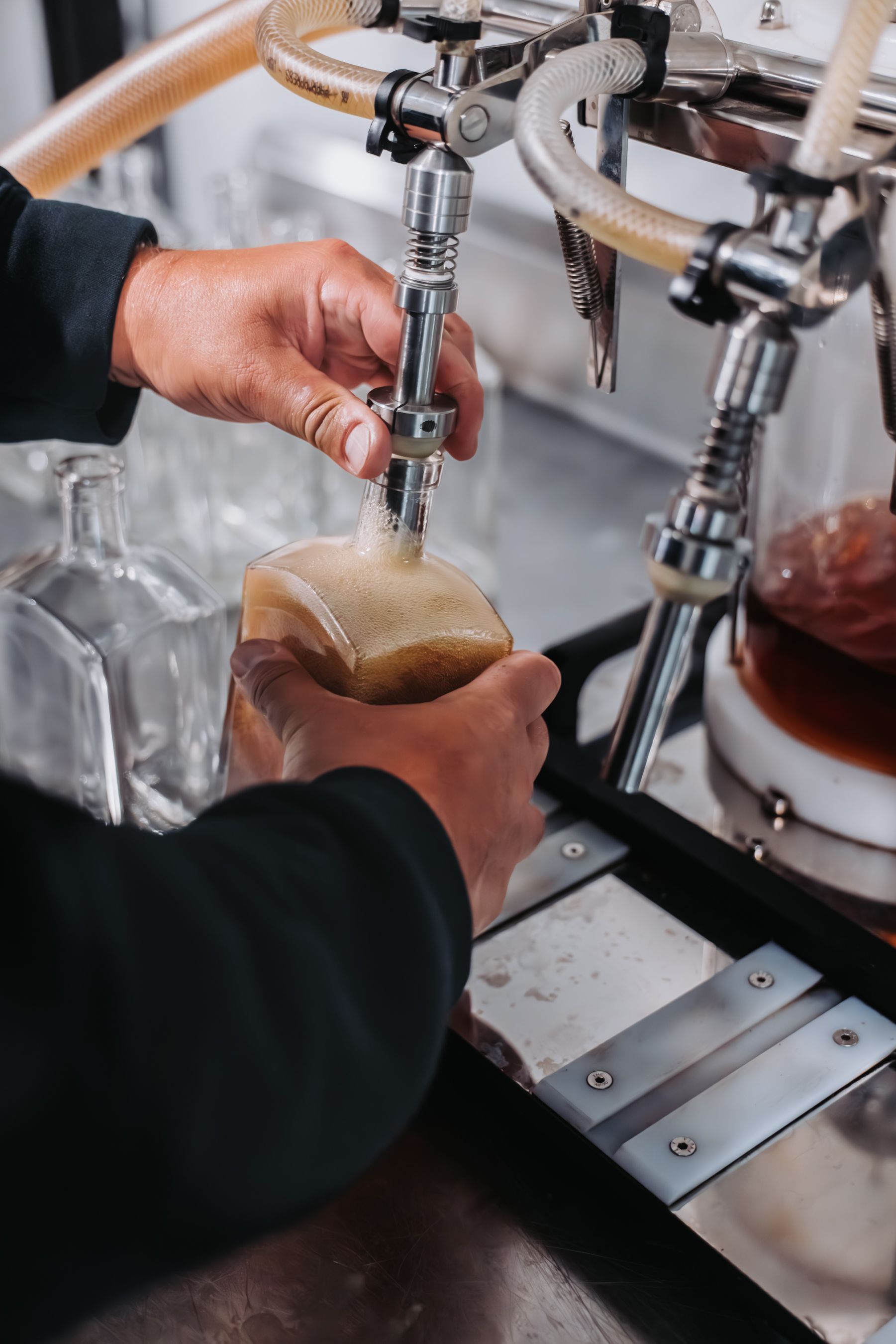 Person pouring from a tap into a square glass, with equipment in the background.