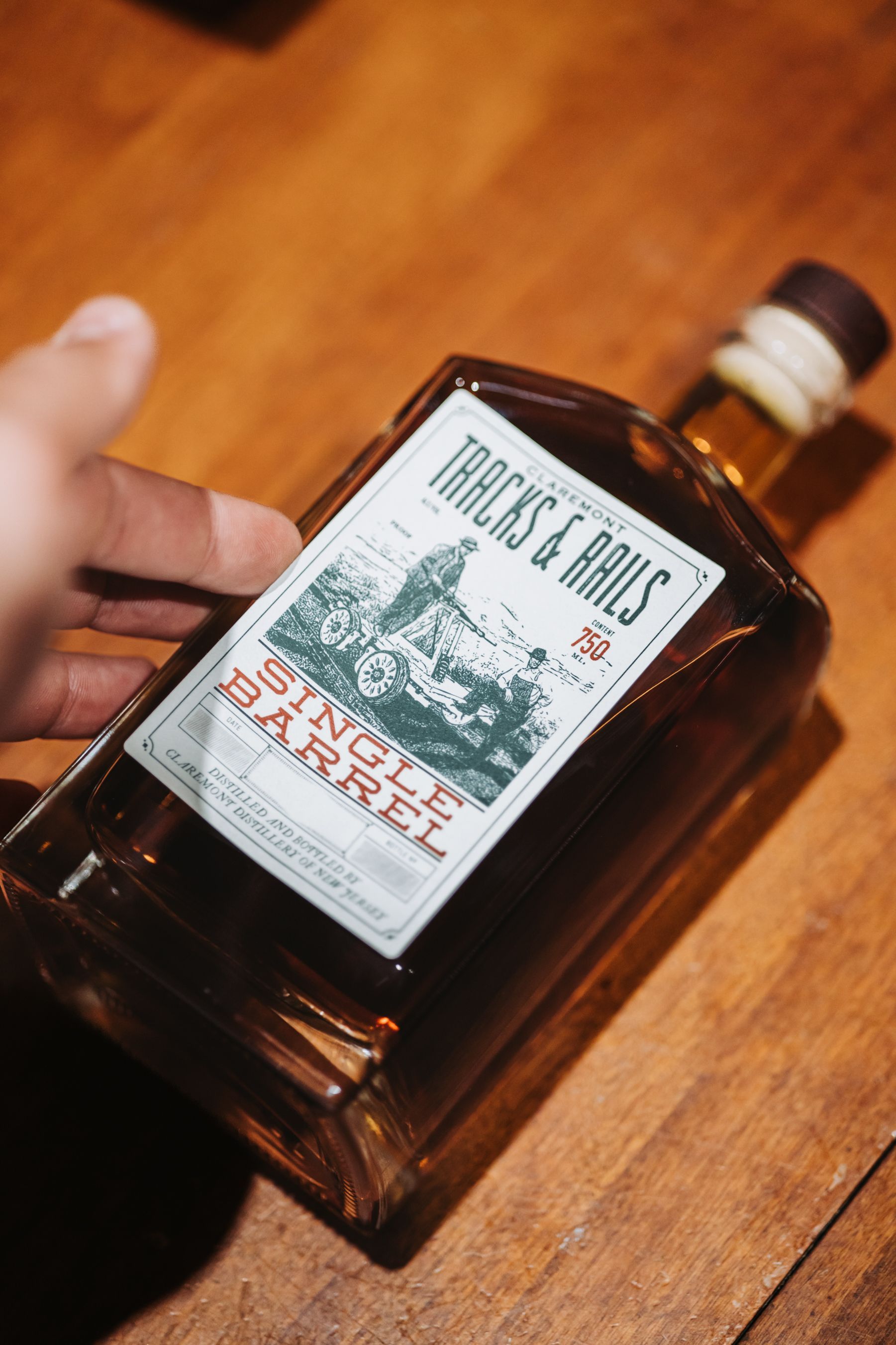 Hand holding a bottle of Tracks & Rails Single Barrel whiskey on a wooden surface.