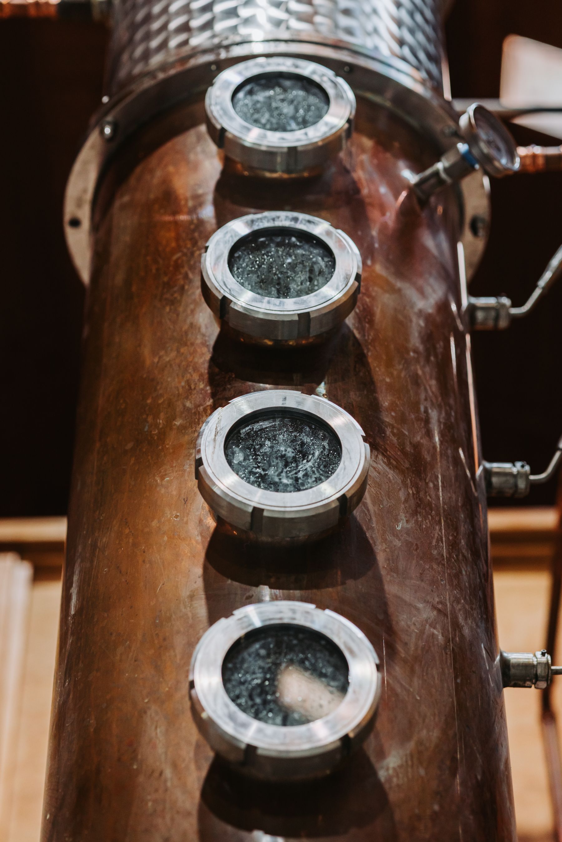 Copper still with four porthole-like windows showing inside workings.