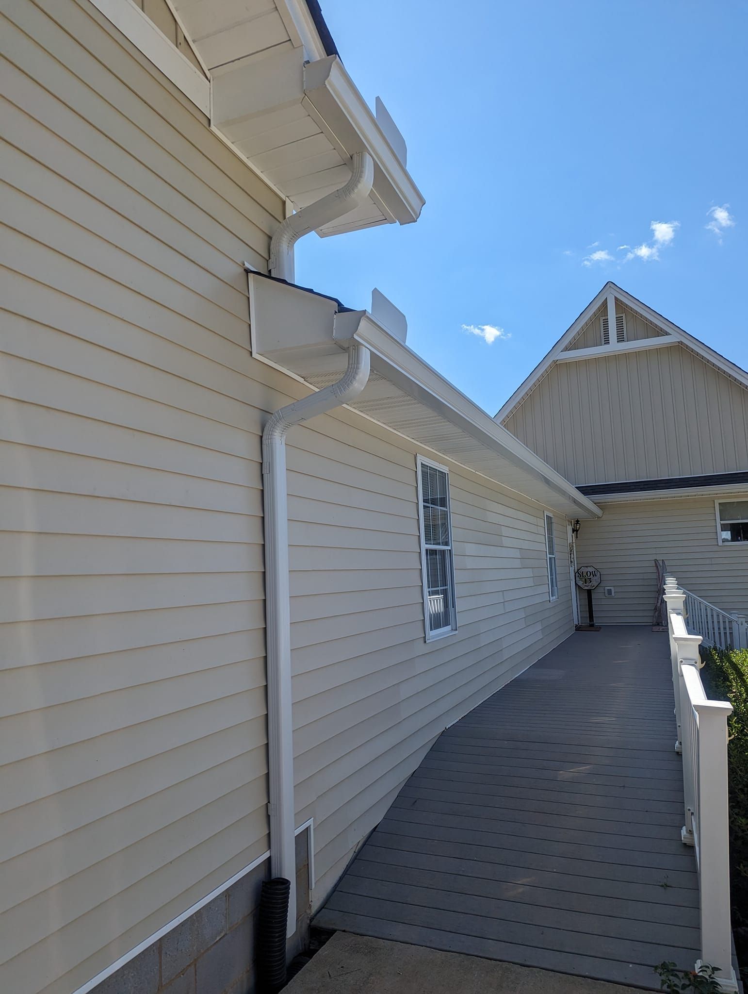 An exterior side view of a light-colored house with a ramp leading along the wall beneath roof gutters.