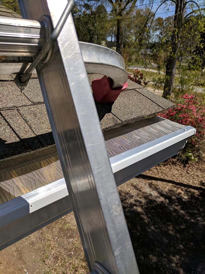 A metal ladder rests against a house roofline, showing a gutter covered with a protective metal mesh screen.