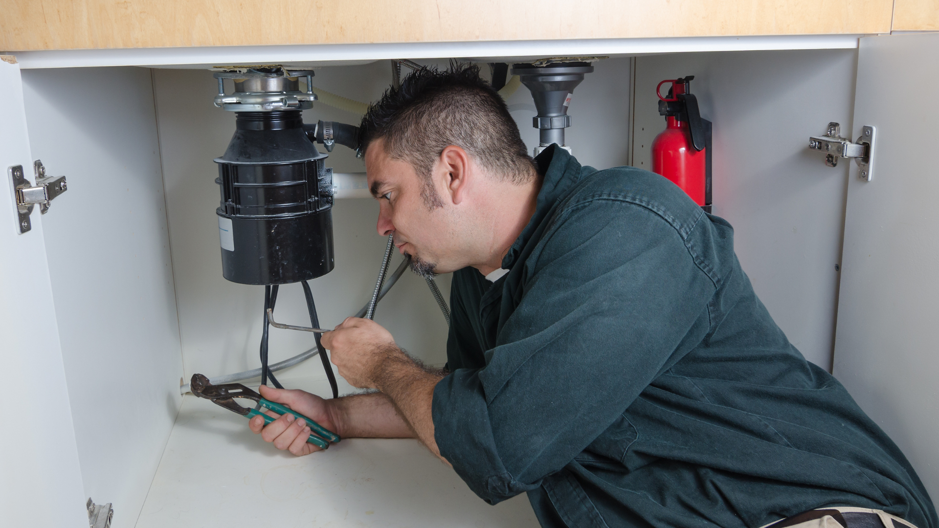 Plumber installing a garbage disposal under a kitchen sink with a screwdriver.