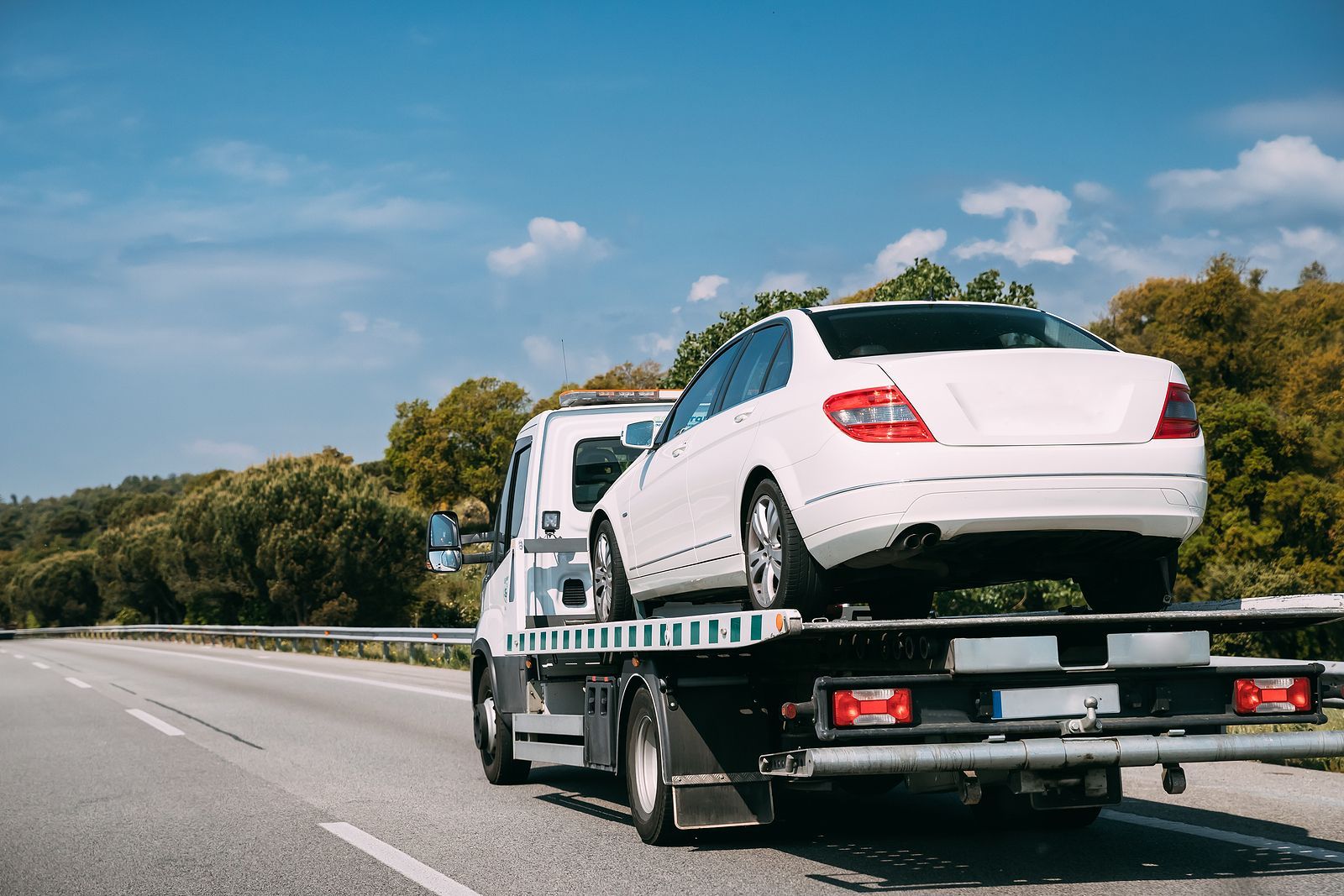 A white car is being towed by a tow truck on a highway.