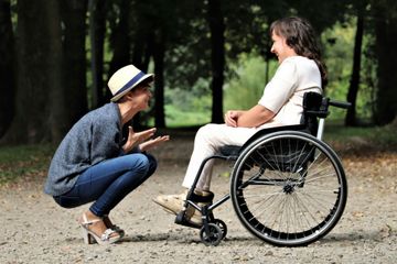 A woman is squatting down next to a woman in a wheelchair.