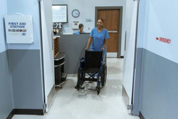 A nurse is pushing a wheelchair down a hospital hallway.