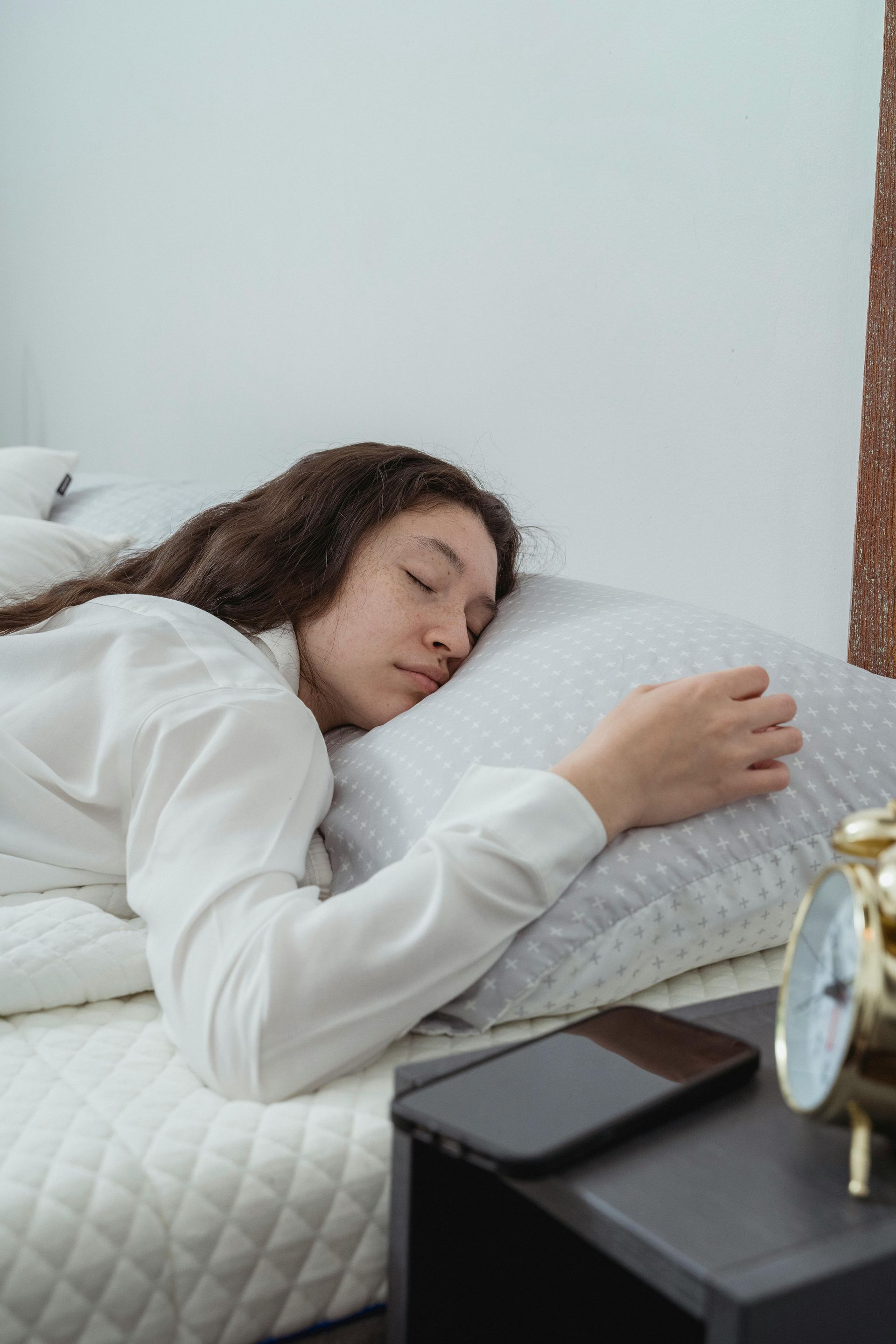 A woman is sleeping on a bed next to an alarm clock.