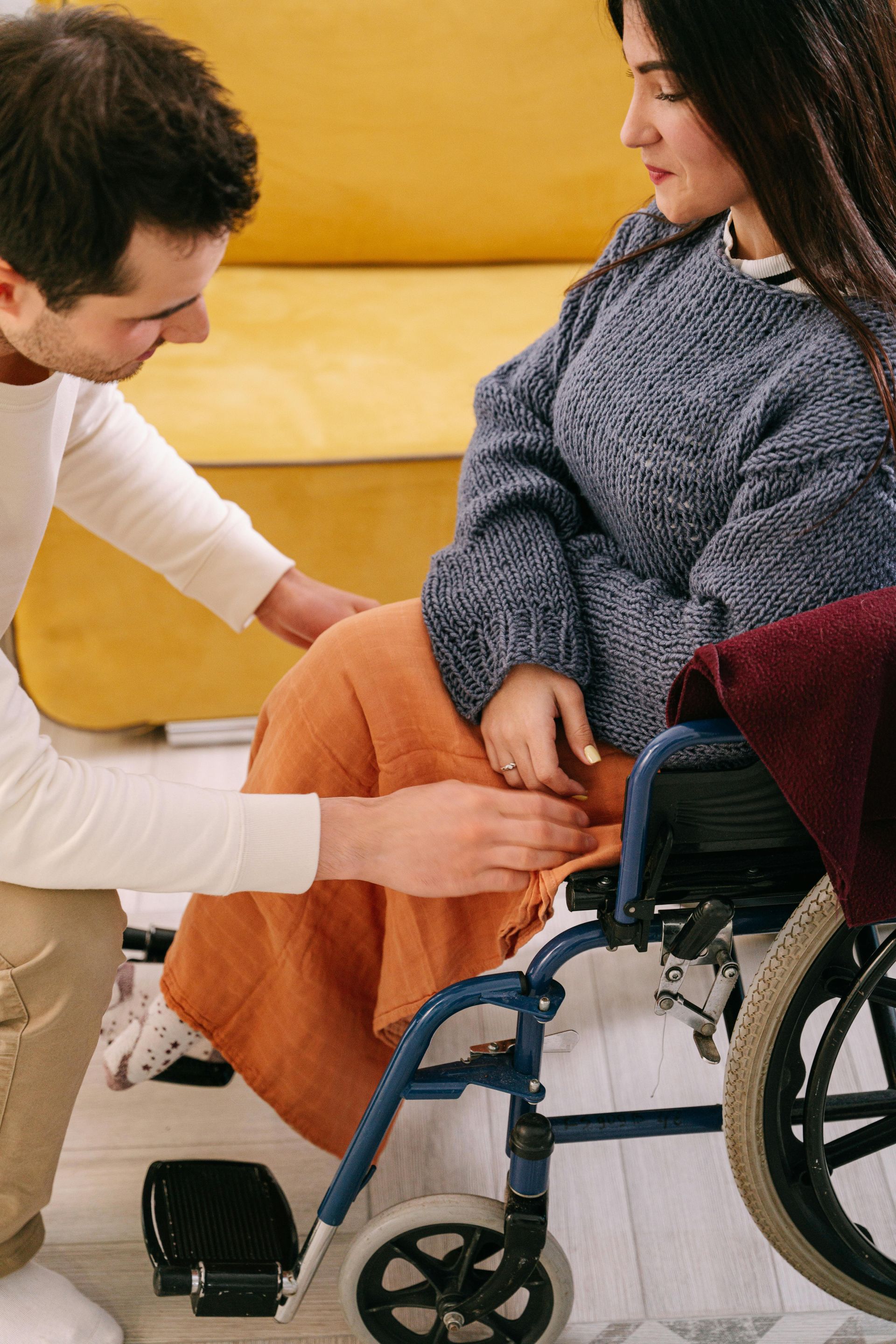 A man is kneeling down next to a woman in a wheelchair.