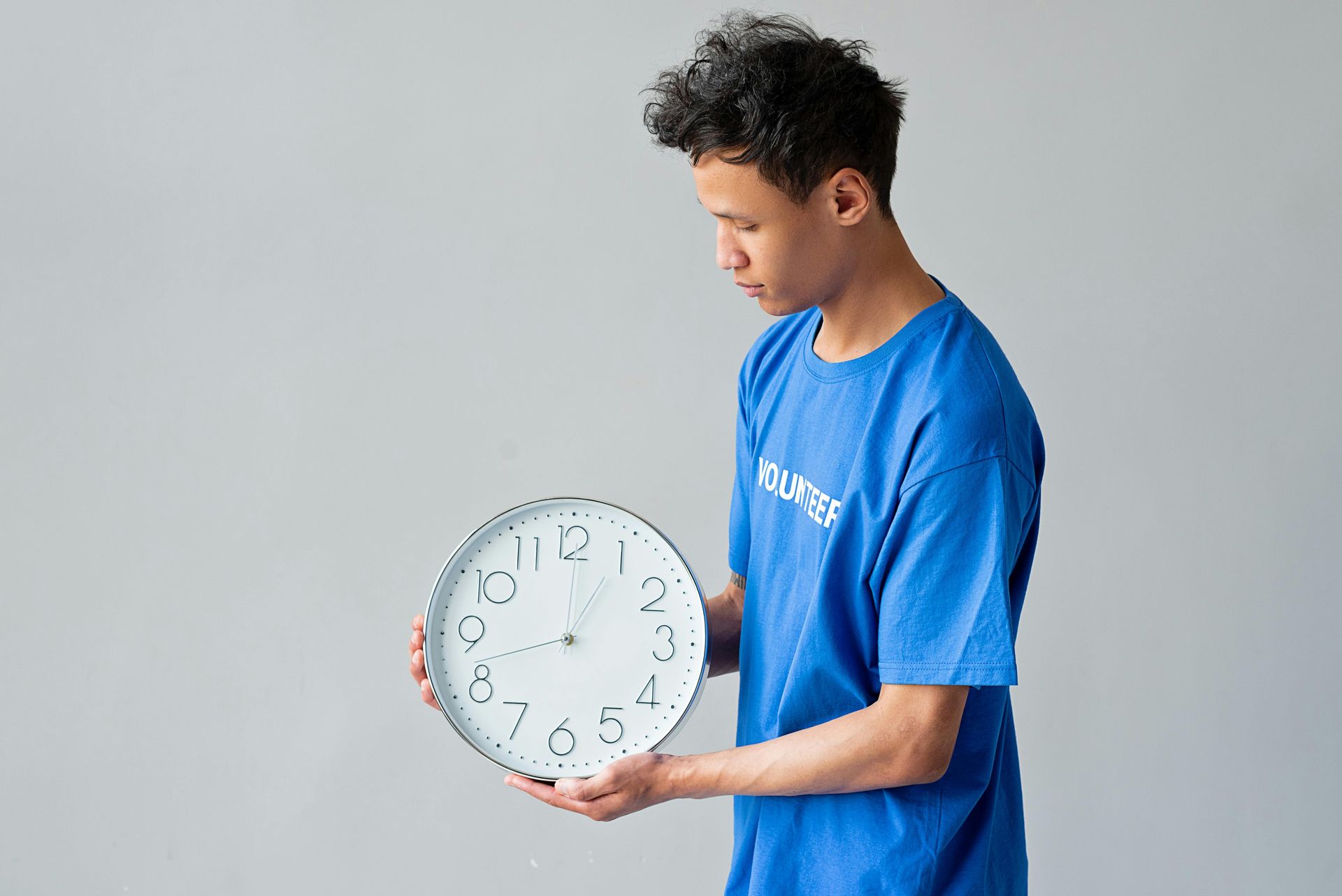 A man in a blue shirt is holding a clock in his hands.