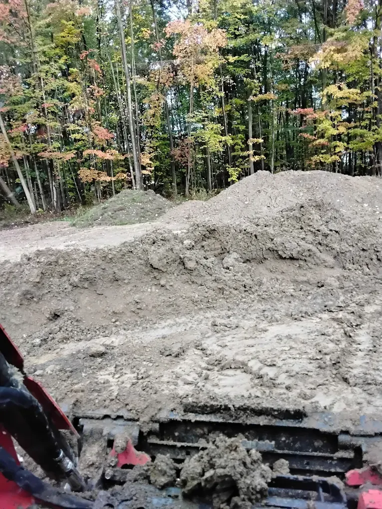 Dirt piles in front of autumn trees, viewed from inside heavy machinery.