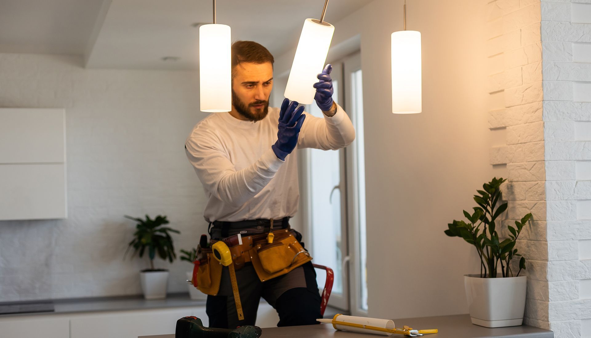 Man in gloves installing light fixture, kitchen setting.