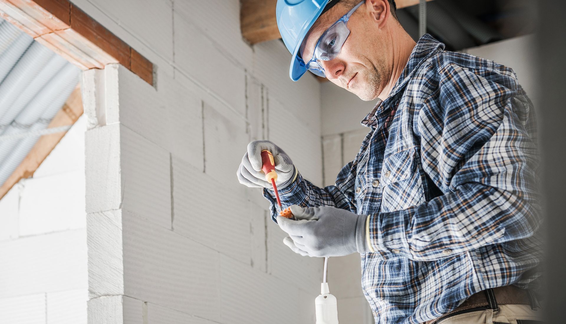Construction worker in hard hat, safety glasses and gloves working on electrical wiring.
