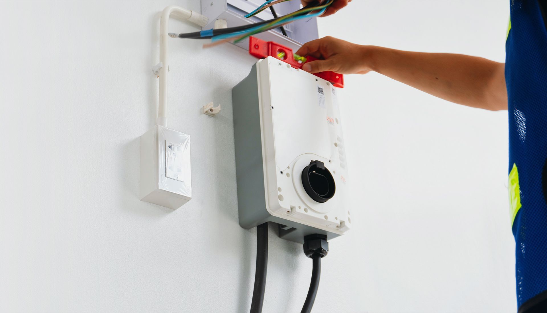 Electrician wiring an electric vehicle charging station on a white wall.