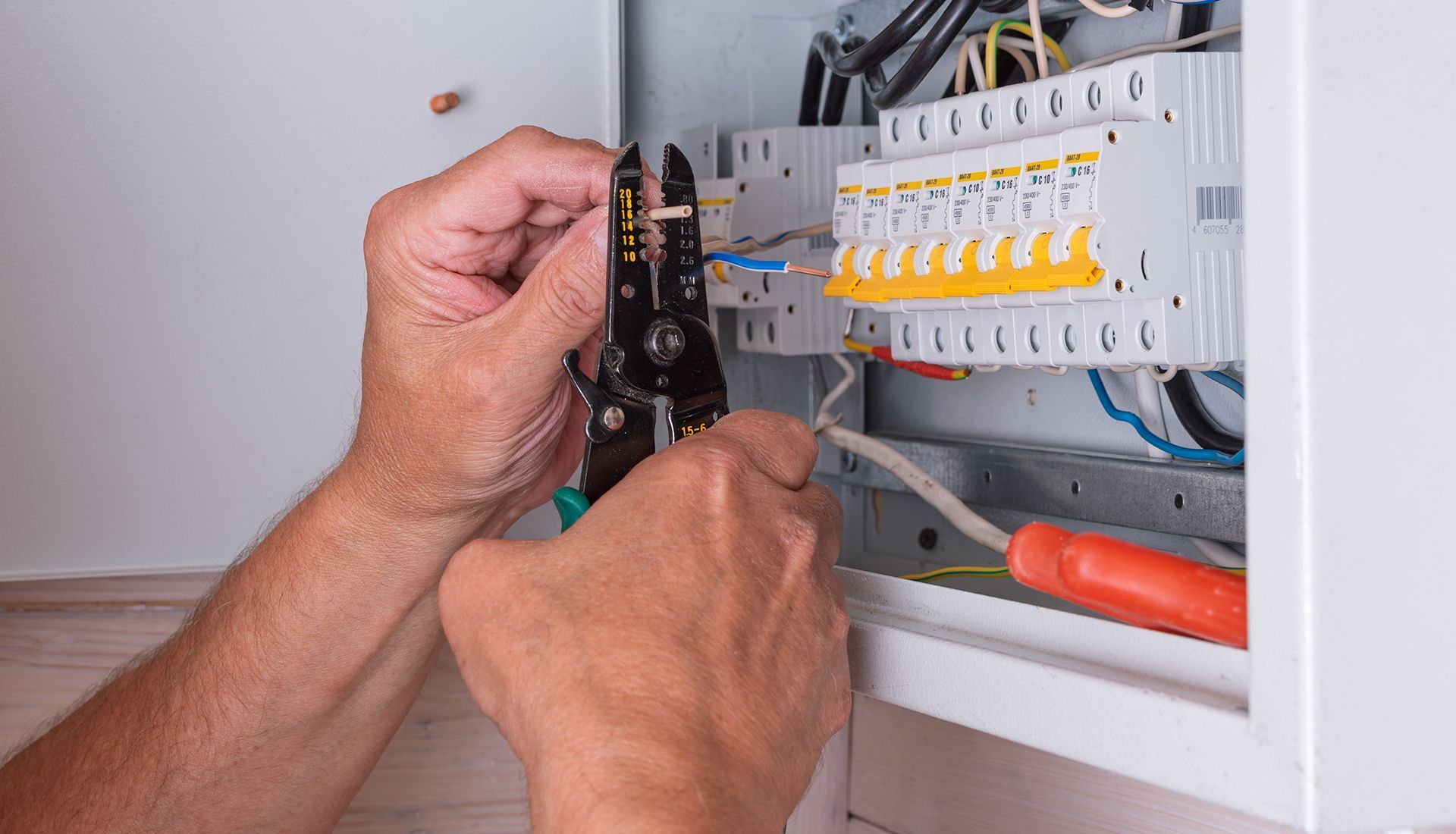 Person using wire strippers to work on electrical wiring in a white panel.