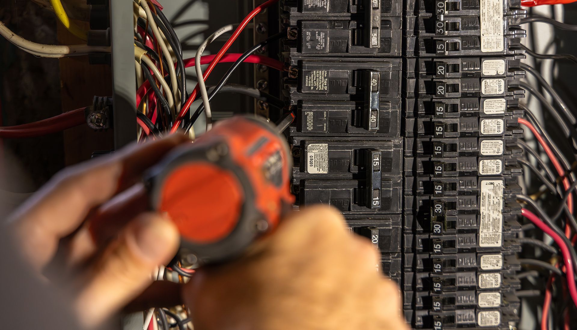 Person using a power tool on a circuit breaker panel with wires.