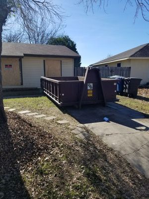 A large red dumpster is sitting on the side of a dirt road.