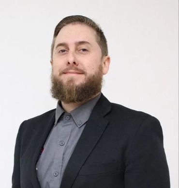 A man with a beard is wearing a suit and a gray shirt.