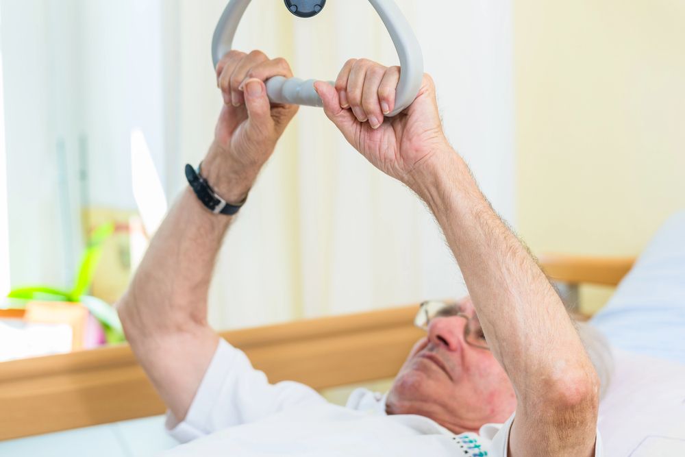 An elderly man is laying in a hospital bed holding a handle.