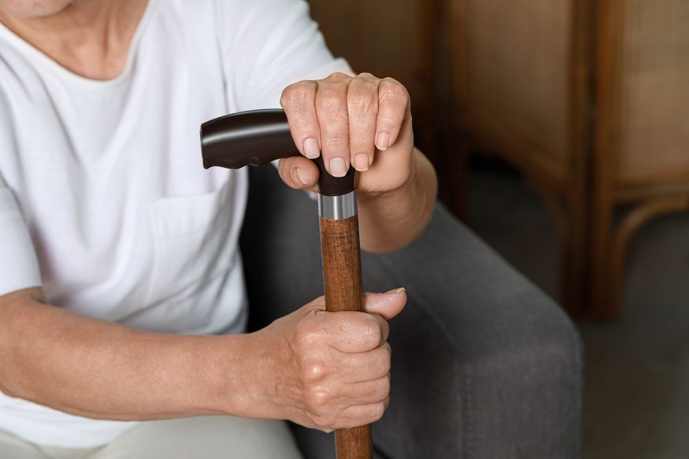 A woman or man in a white shirt holding the handle of a quad cane with both hands.