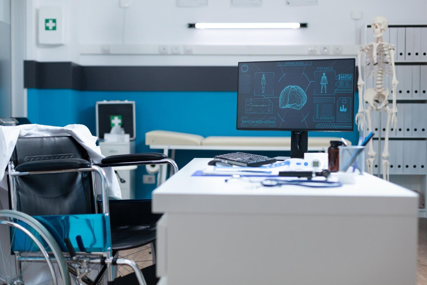 A doctor 's office with a wheelchair and a computer on the desk.