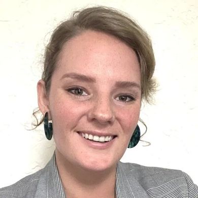 A woman wearing a gray jacket and green earrings is smiling for the camera.