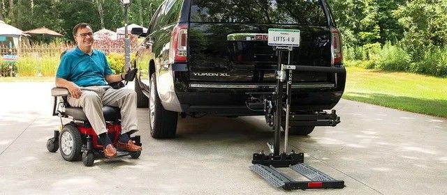 A man in a wheelchair is sitting next to a car.