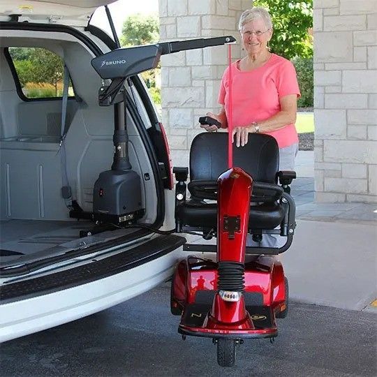 A woman in a pink shirt is standing next to a red mobility scooter