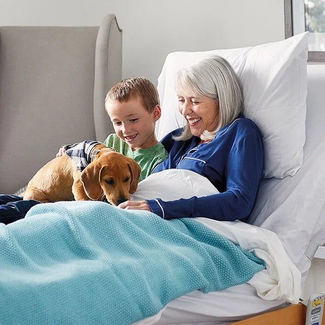 A woman and child are laying in a hospital bed with a dog