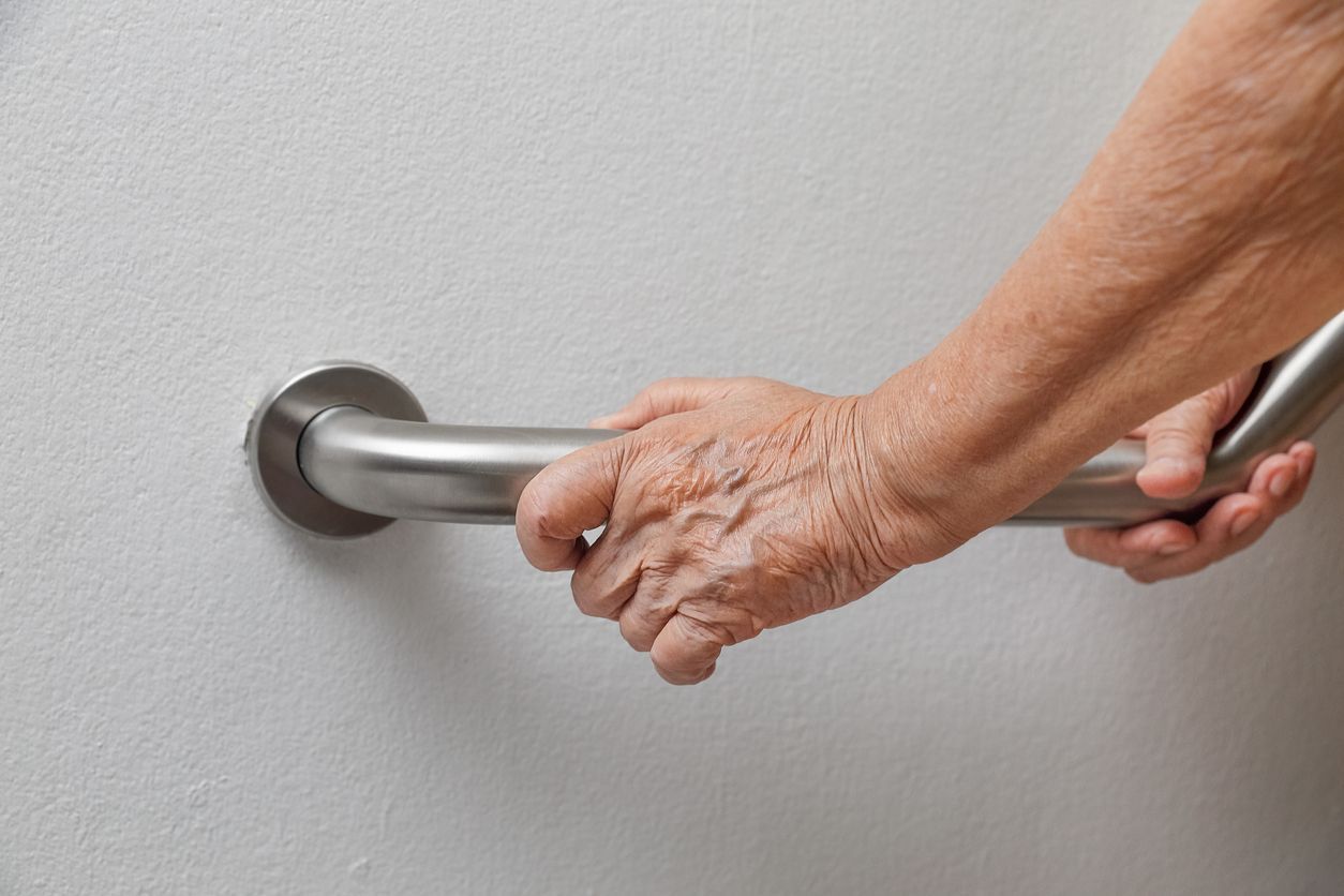 An elderly woman is holding onto a stainless steel hand rail.