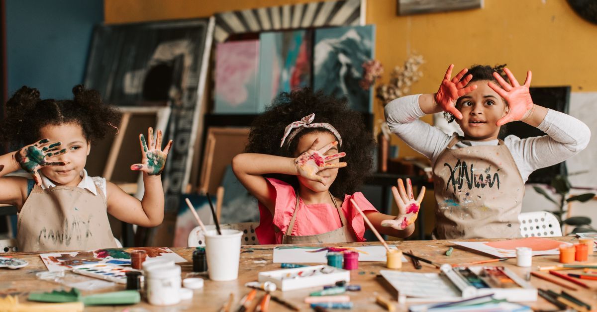 Children making handmade Veterans Day cards with colorful painted handprints on a table.