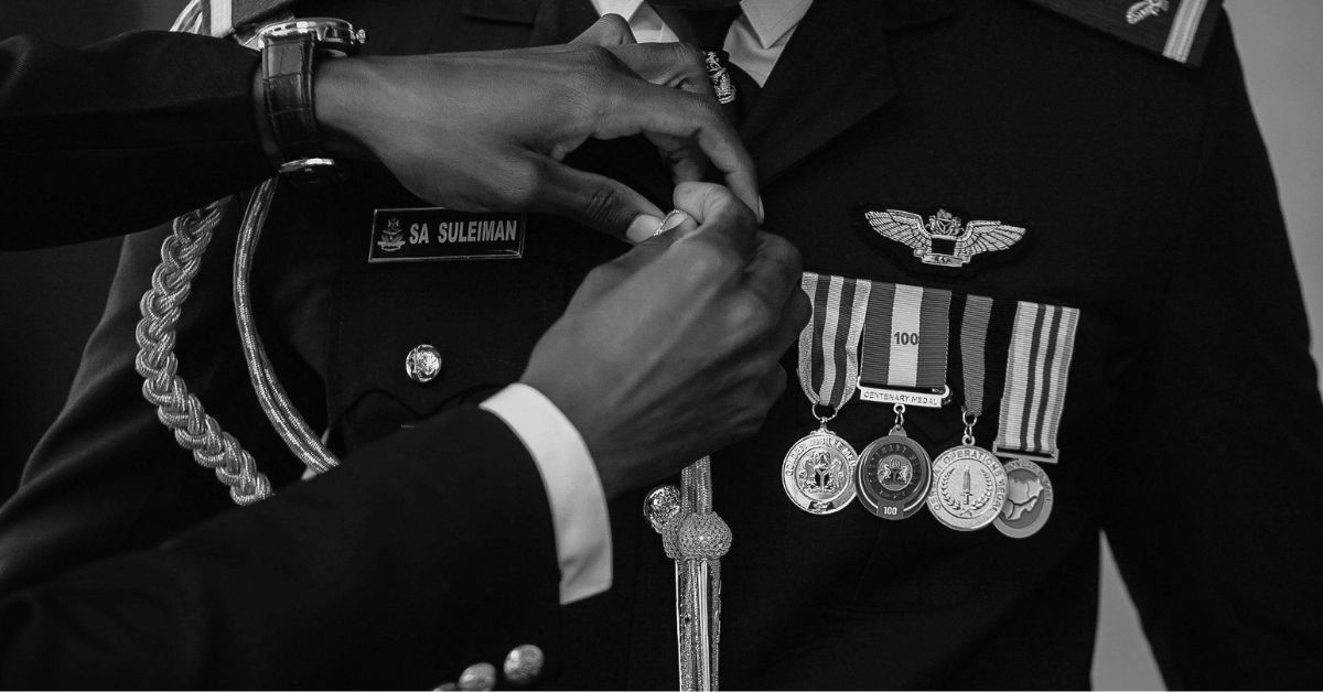 A black and white close-up of a high-ranking officer in a formal military dress uniform with wings and multiple medals, having a new decoration pinned to their chest.