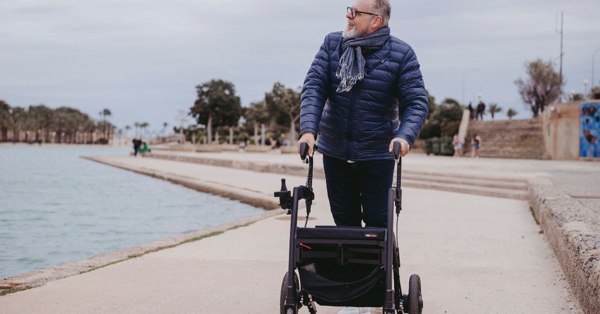 Senior man using an outdoor walker while walking along a waterfront path